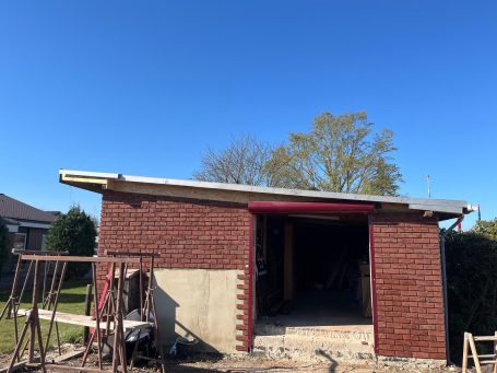 Rohbau eines Hauses mit roten Klinkerriemchen, blauer Himmel und Bäume im Hintergrund.