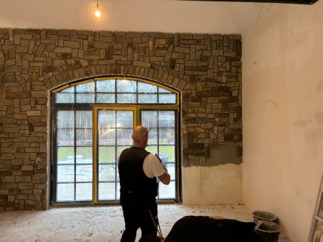 Mann betrachtet einen Raum mit Steinwand und großen Fenstern.