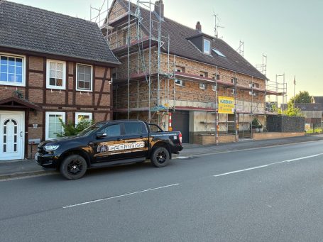 Ein schwarzes Firmenfahrzeug parkt vor einem mehrstöckigen Haus mit Gerüst und Bauarbeiten.