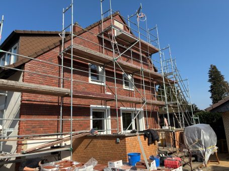Rote Klinkerriemchen mit Gerüst und Baustellenmaterial, unter blauem Himmel.
