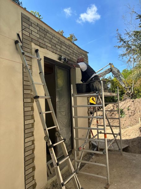 Ein Handwerker arbeitet auf einer Leiter an einer Wand eines Hauses.