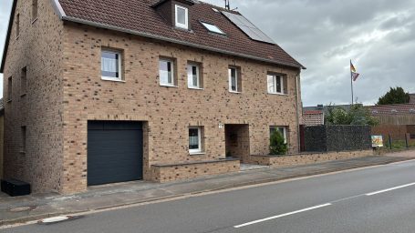 Zwei­stöckiges, geklinkertes Haus mit Garagen­tür und Fahne vor dem Eingang.